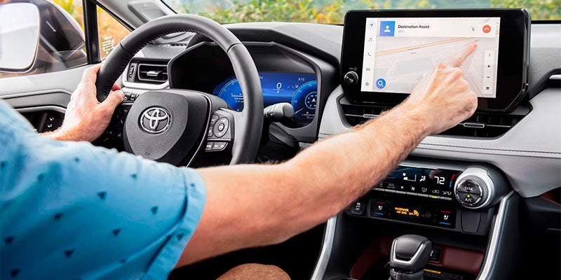 A person's hands gripping the steering wheel and touching the navigation screen in a modern Toyota car.