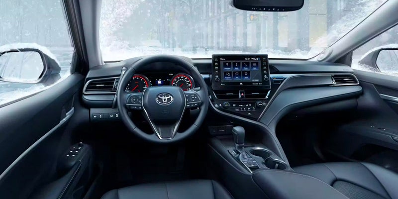 Interior view of a modern car in black and gray, with a steering wheel and digital dashboard, snowy outside.