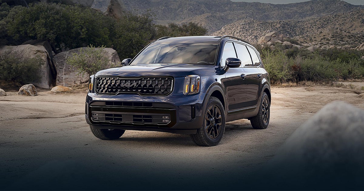 Dark blue Kia Telluride SUV on mountain road with scenic backdrop