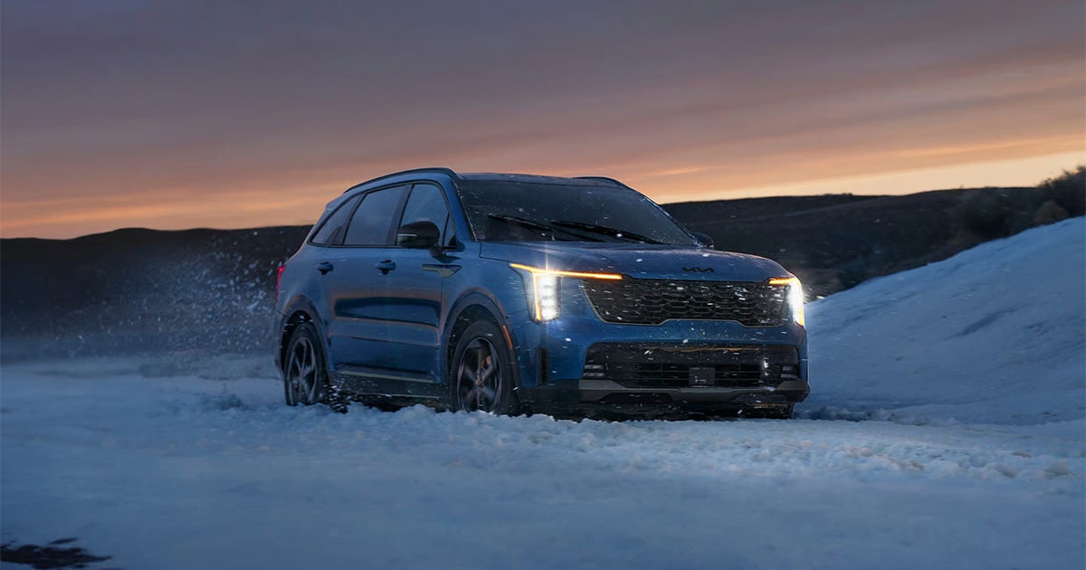 Blue Kia Sorento Hybrid SUV in snowy winter landscape at sunset
