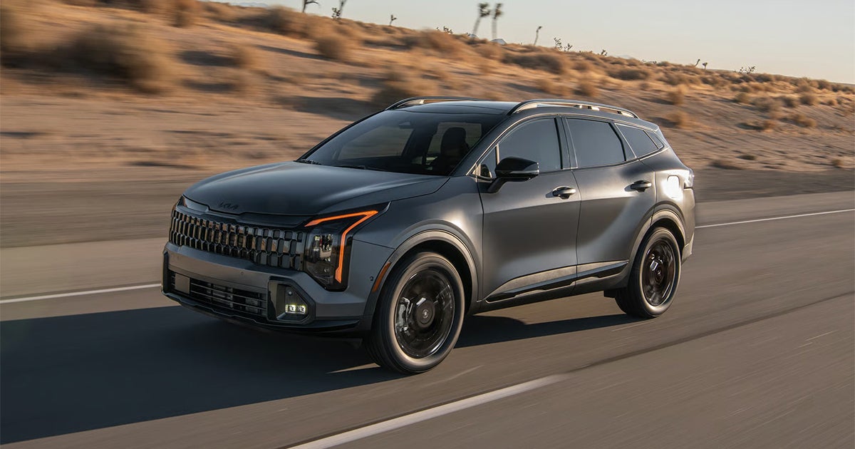 Dark Kia Sportage SUV driving on desert highway with orange accent lighting