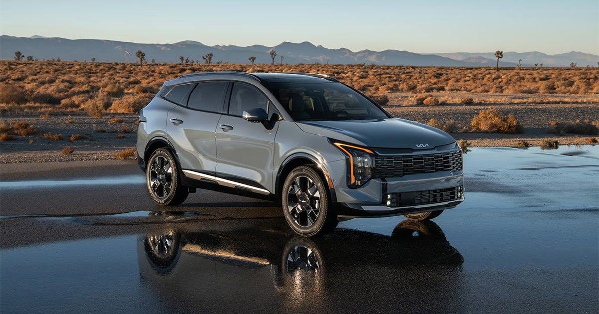 Silver Kia Sportage SUV with reflection on wet desert pavement at sunrise