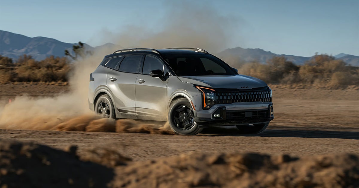 Silver Kia Sportage SUV kicking up dust cloud on desert off-road trail