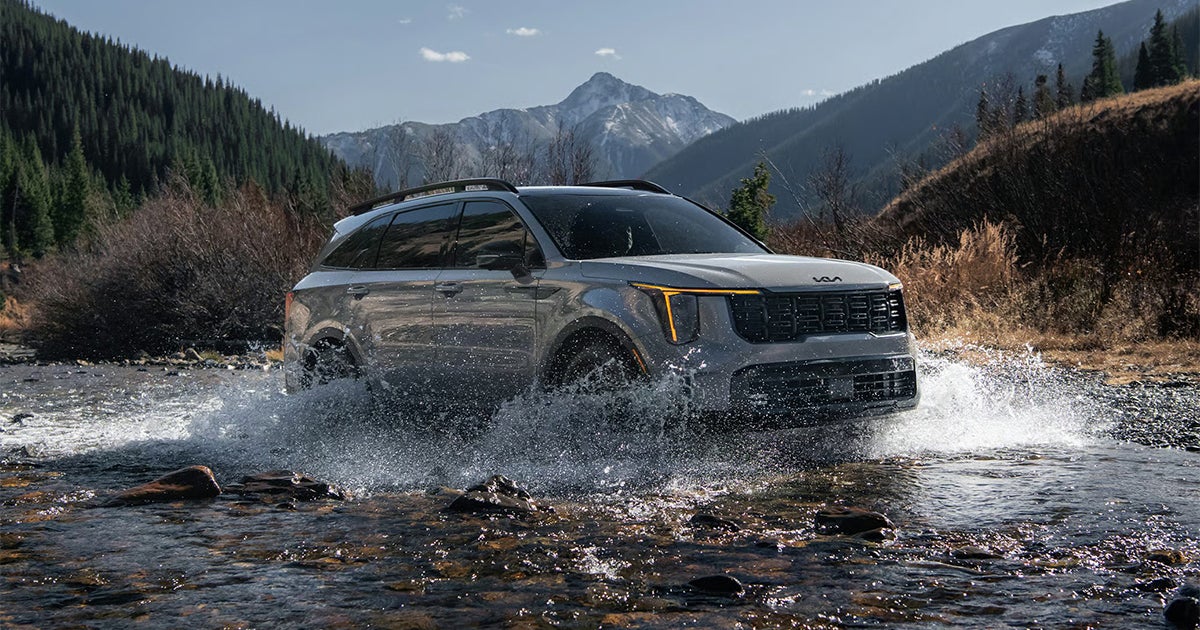 Silver Kia Sorento SUV crossing mountain stream with water splashing