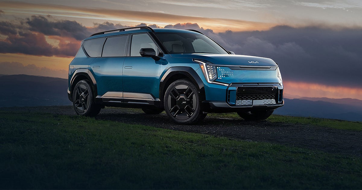 Blue Kia EV9 electric SUV positioned on hillside at golden hour sunset