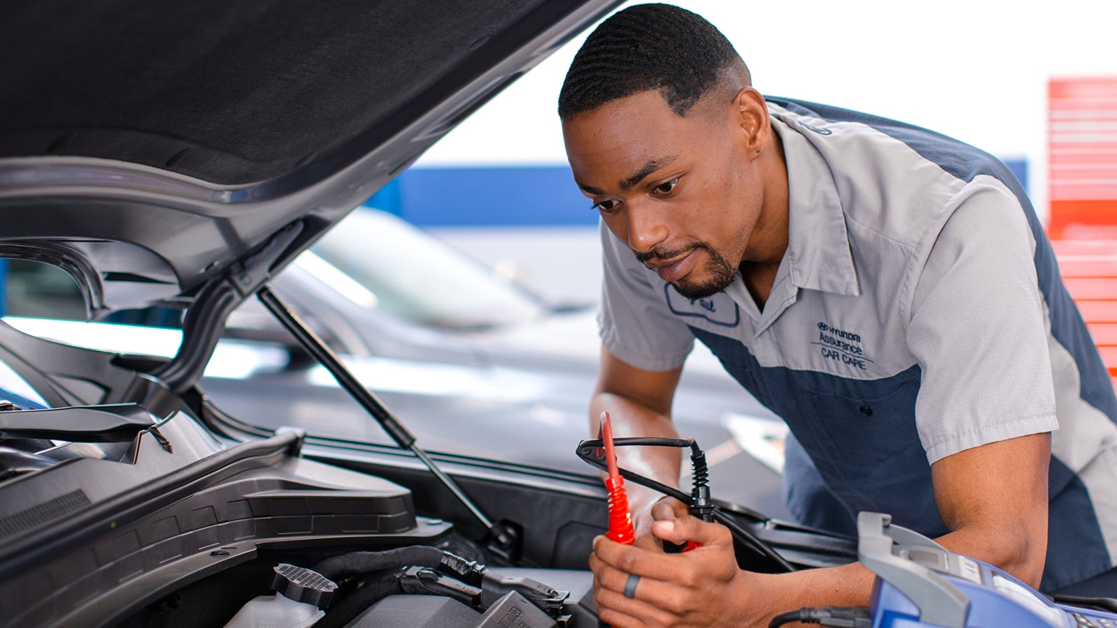 Hyundai technician testing a vehicle battery under the hood