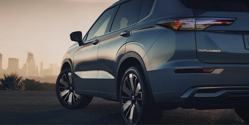 A photo of the drivers side of a 2025 Mitsubishi outlander with a cityscape in the backround.