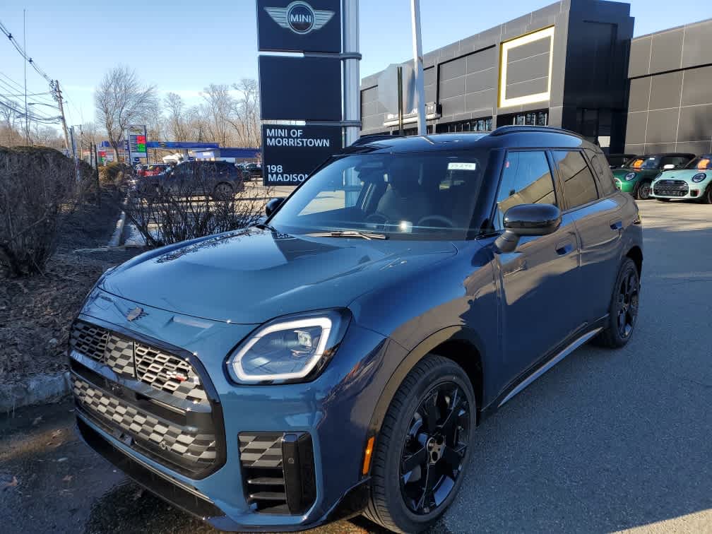 A blue 2026 MINI Countryman All4 parked outside a dealership, with a modern building in the background.