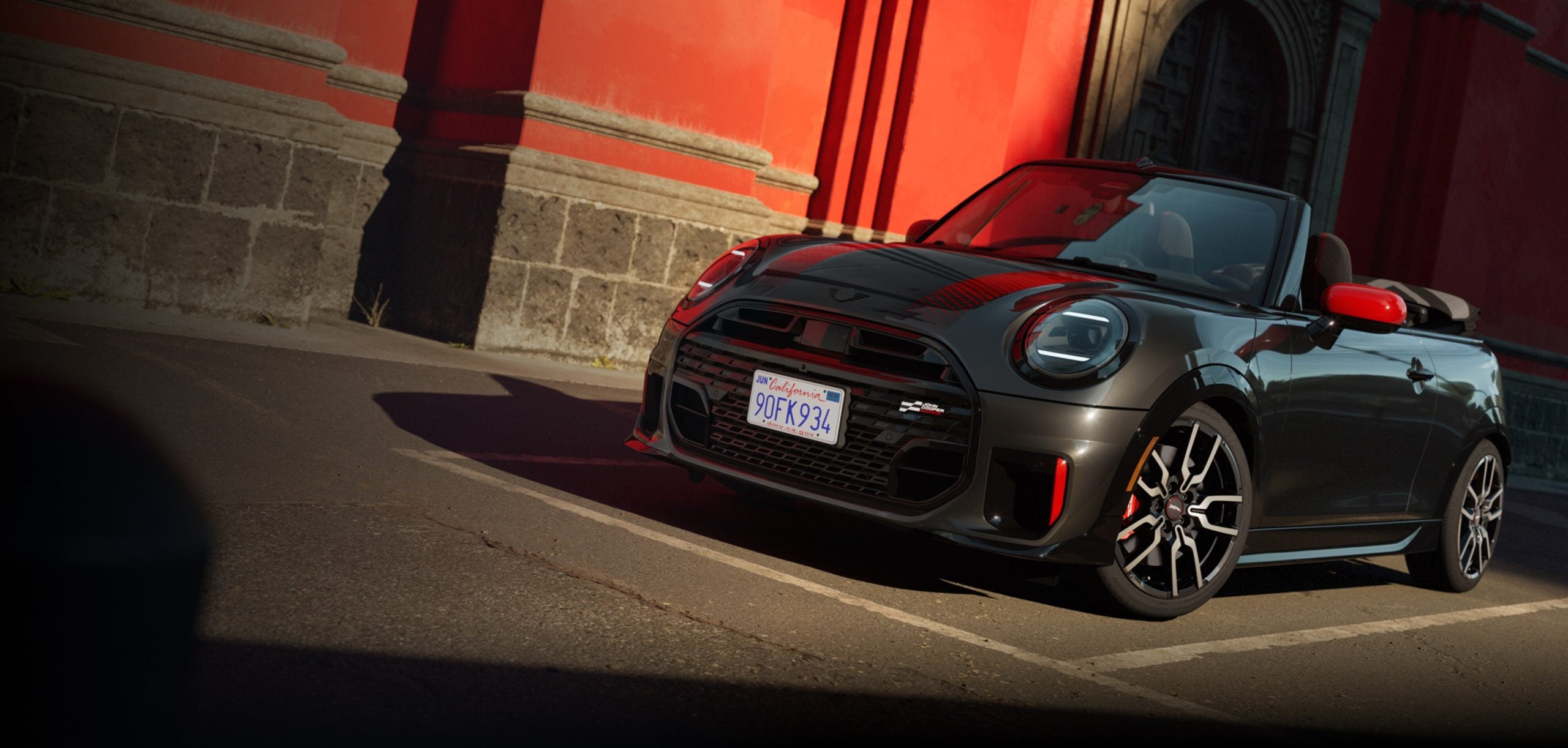 A sleek 2025 MINI John Cooper Works convertible car parked on the street, featuring a red and black design.