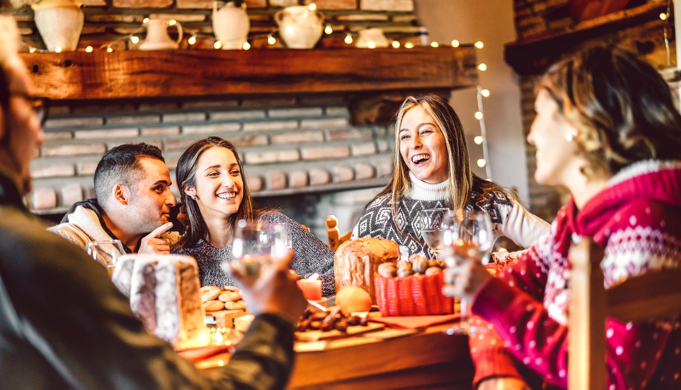 Millenial people tasting Christmas sweets at home supper party - New year's eve and winter holiday concept with young friends having fun eating together at evening - Bulb string lights warm filter