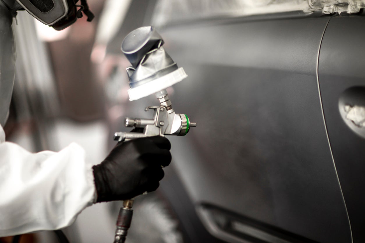 Car painter in white overalls spraying a car body with paint.