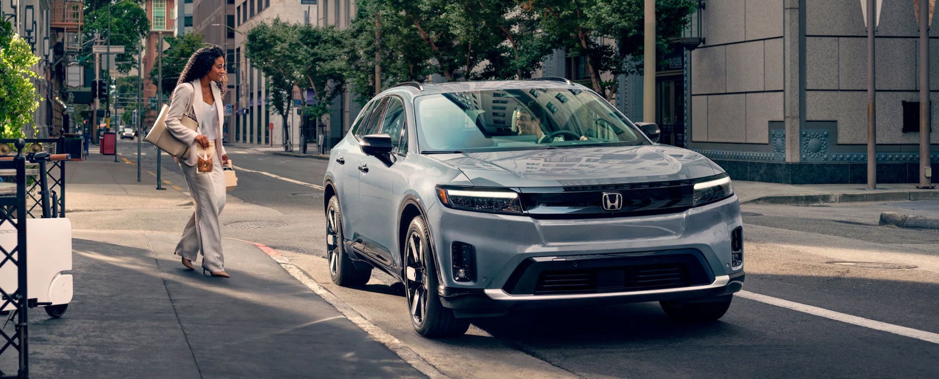 A woman walking to the passenger side of a silver Honda vehicle parked in a city street