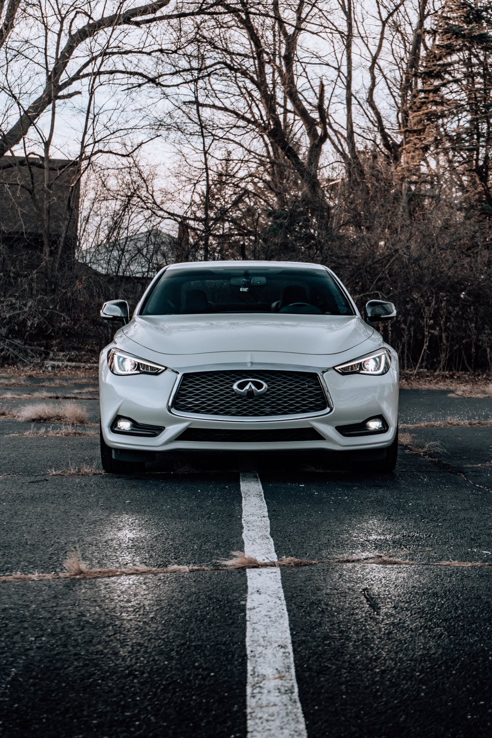 A white Infiniti car parked in a parking lot over the line with its lights on