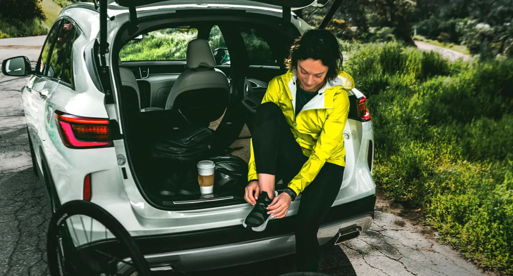 A 2021 Infiniti QX50 with the trunk open and a woman sitting inside tying her shoes