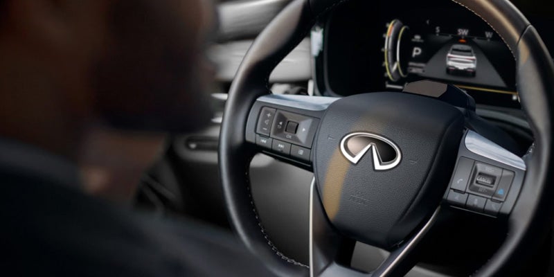 Close-up of an Infiniti steering wheel inside a vehicle, showing the driver’s hands and digital instrument cluster.