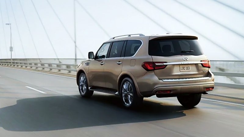 Gold Infiniti Q80 SUV driving on a bridge.
