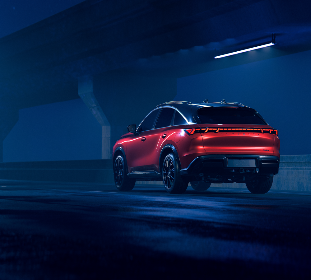 Red 2027 INFINITI QX65 SUV with illuminated tail lights under a dimly lit overpass.