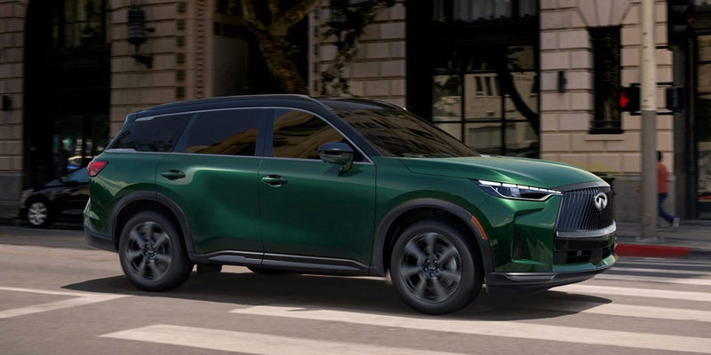 Green Infiniti QX60 SUV driving through a city street.