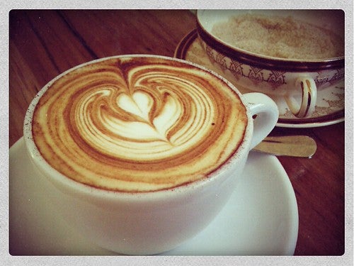Cappuccino with latte art heart drawn in it and bowl of sugar in the background
