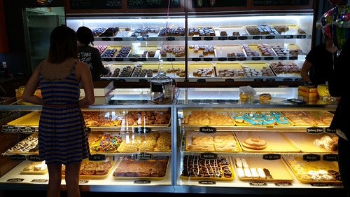 Someone shopping for donuts in lit display case photographed from behind from behind