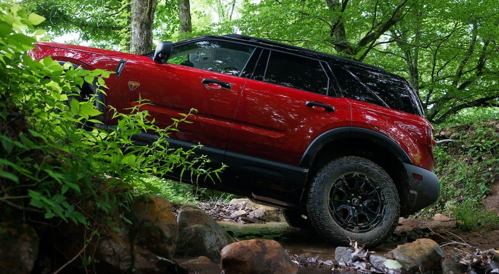 Side of a red 2026 Ford Bronco Sport driving off-road in a forest.