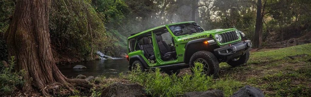 Bright green Jeep Wrangler Rubicon parked in a forest next to a stream.