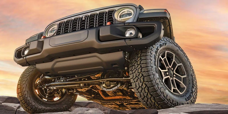 Low-angle front view of a Jeep Gladiator on rocks at sunset.
