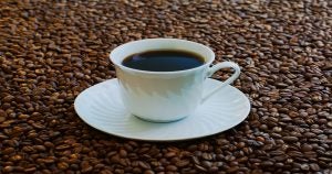 Coffee inside of a whit mug on top of a white saucer sitting on coffee beans | Ellisville, MO