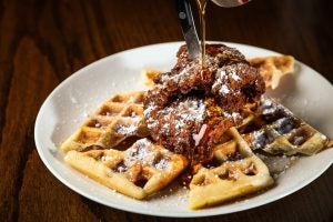A white plate of chicken and waffles with powdered sugar and syrup.