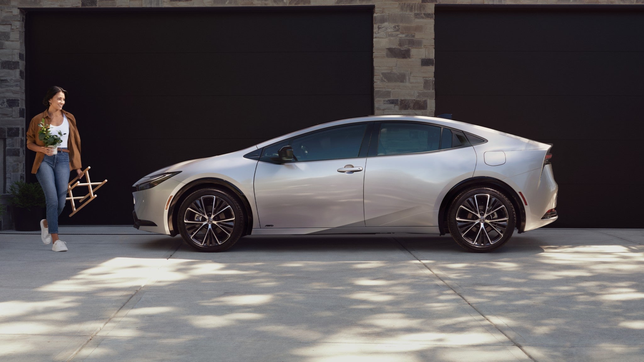 A gray Toyota Prius parked in front of a garage with a woman walking in front of it.