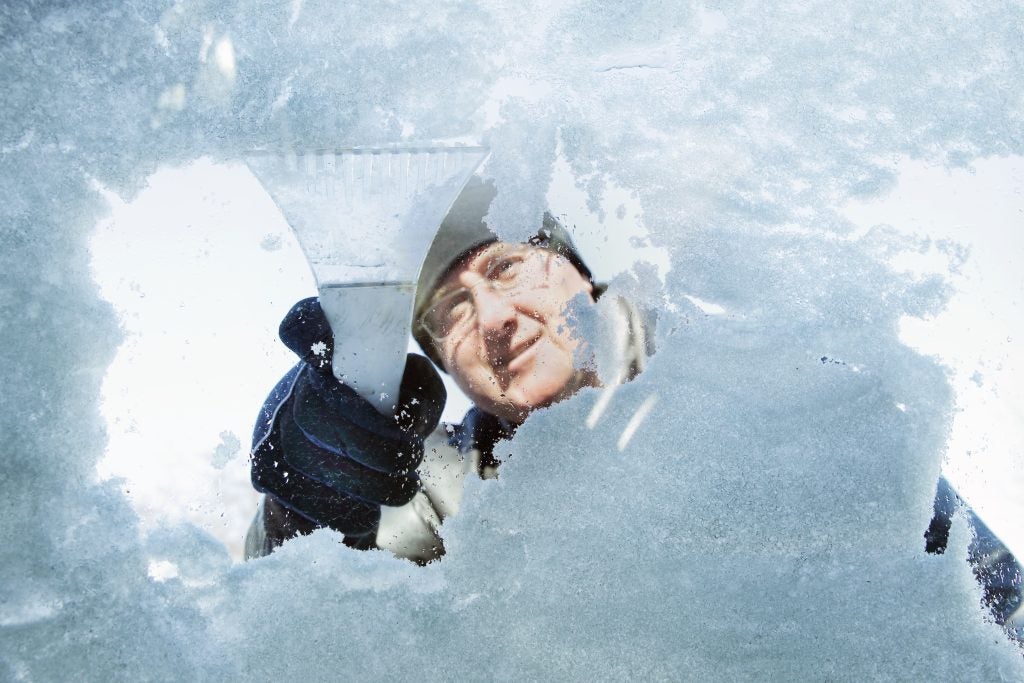 Man scrapping snow and ice off windshield