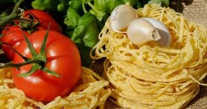 A board filled with Italian cooking ingredients including pasta, garlic, and basil.