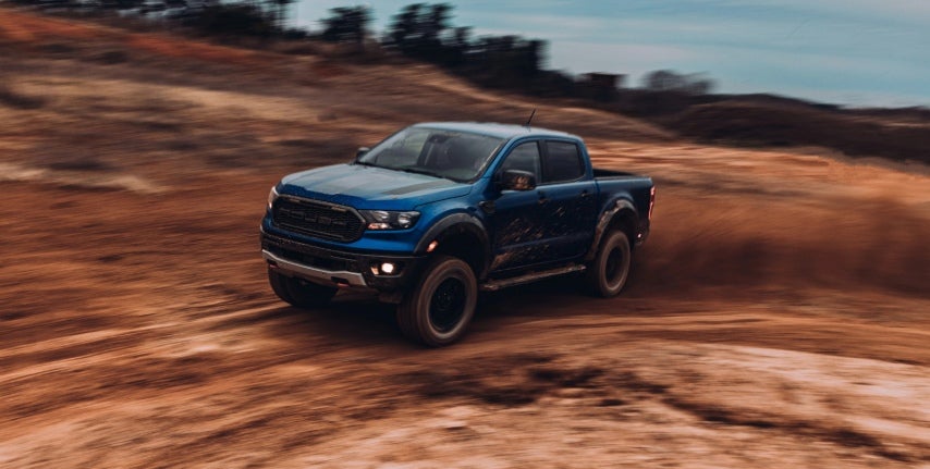 Blue Ford F-150 Roush kicking up dirt while drifting on a rugged off-road trail at dusk.