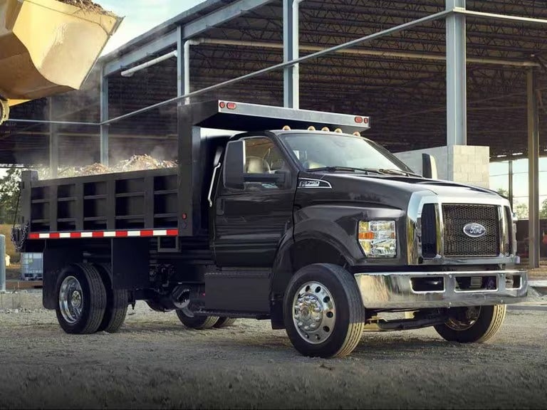 Black Ford dump truck loaded with gravel parked at a construction site near a partially built steel structure.