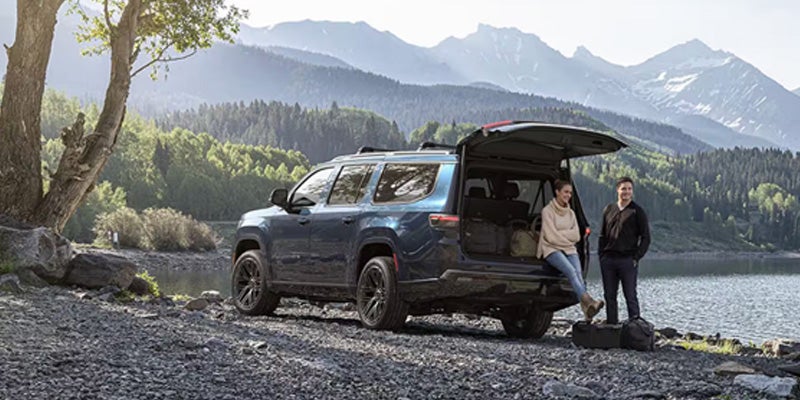 Blue SUV parked by a mountain lake with two people standing near the open trunk.