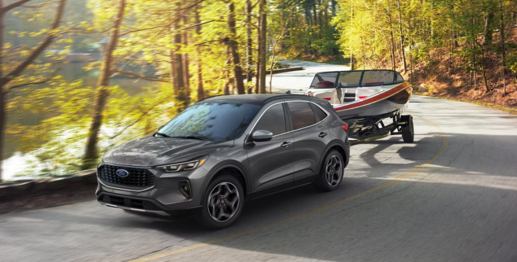 The 2026 Ford Escape tows a boat behind it on a fally road. 