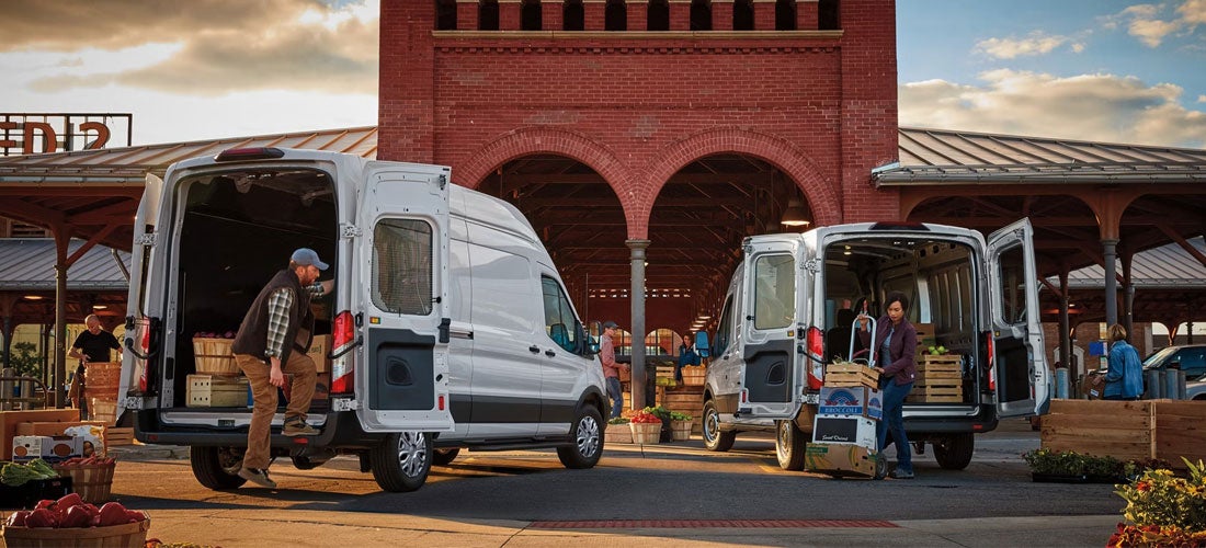 High-roof 2027 Ford Transit cargo vans parked at a loading dock with rear doors open for commercial delivery.
