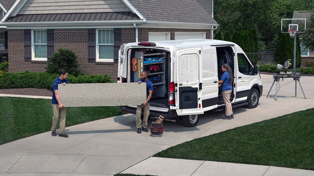 Contractors loading materials into an upfitted Ford Transit cargo van with custom storage shelving.