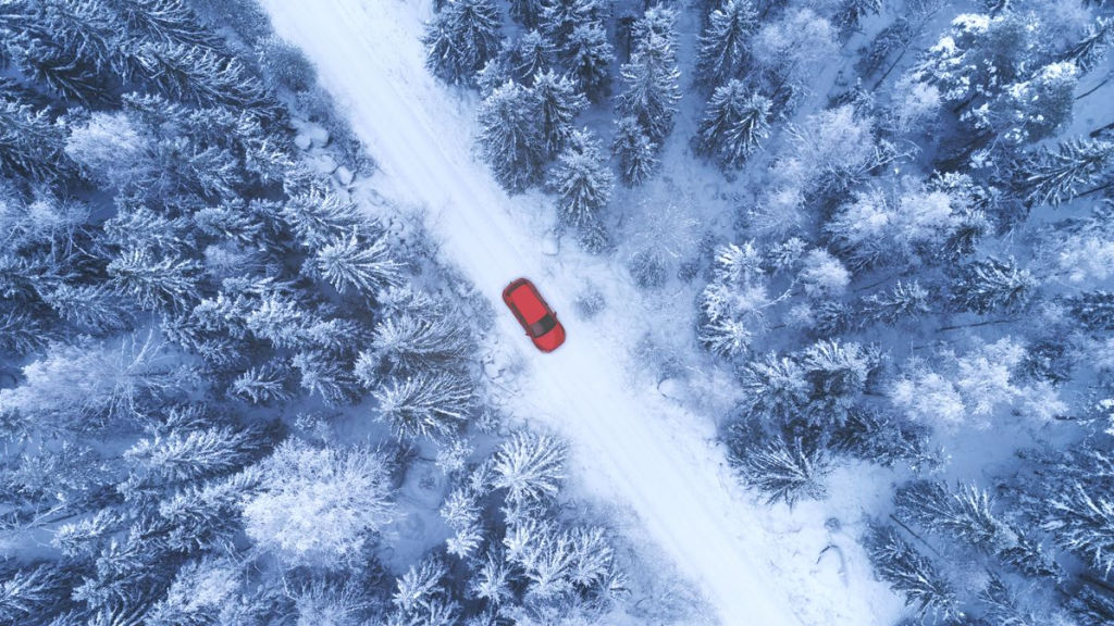 A red car driving down a snow covered road.