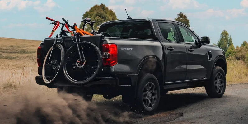 A black 2026 Ford ranger with Mountain bikes in the back driving down a dirt road.