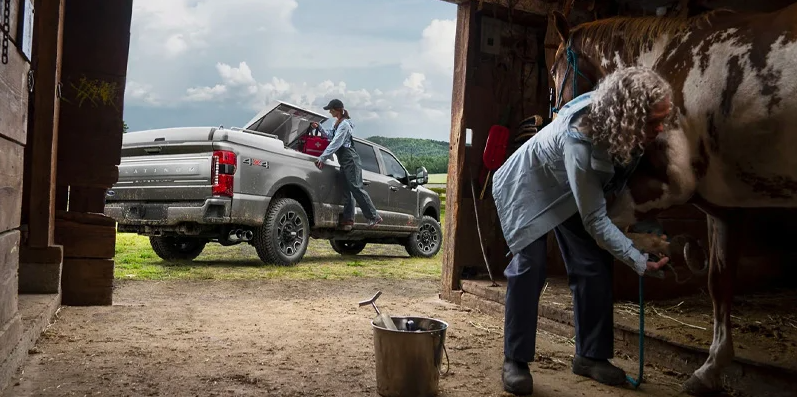 A photo of a 2025 Ford F-250 parked next to a stable where someone is taking care of a horse.