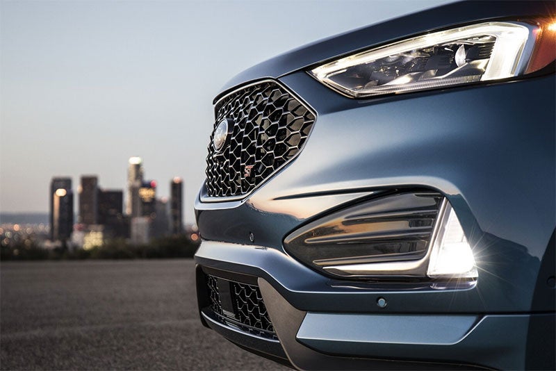 Close-up of a car's grille and headlights with a city skyline in the background.