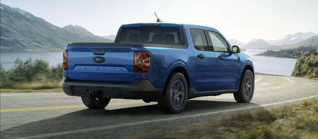 A blue 2025 Ford Maverick driving down a road toward a lake.