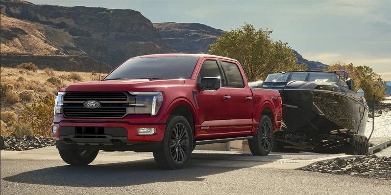 A red Ford F-150 driving down a ramp to launch a boat it is towing.