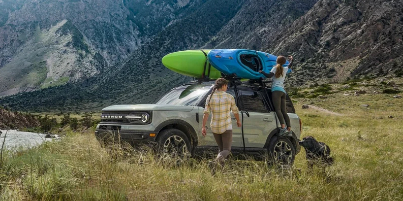 A woman strapping down kayaks on the top of a 2024 Ford Bronco Sport.