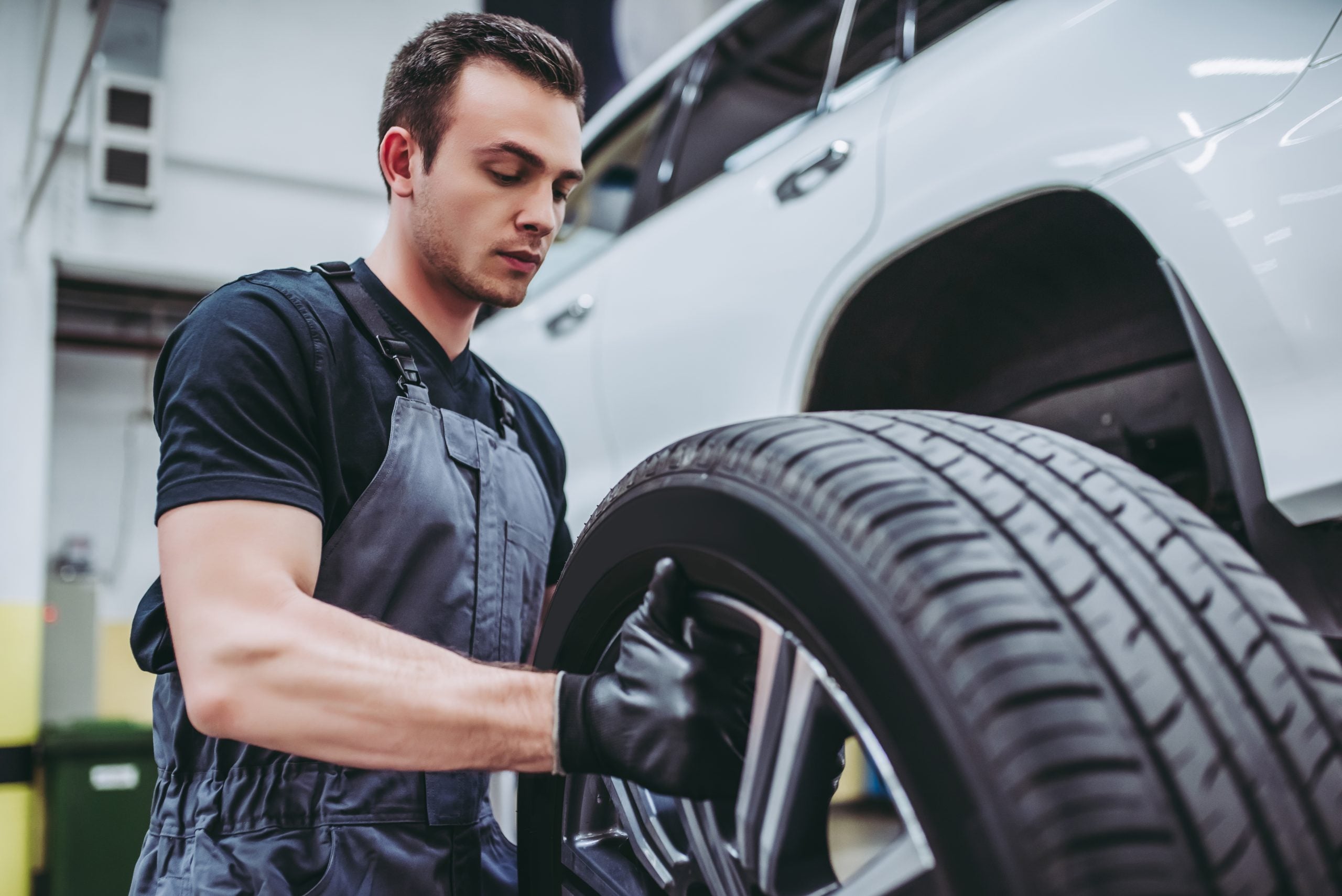 A mechanic wearing gloves installs a tire on a vehicle in an auto repair shop.