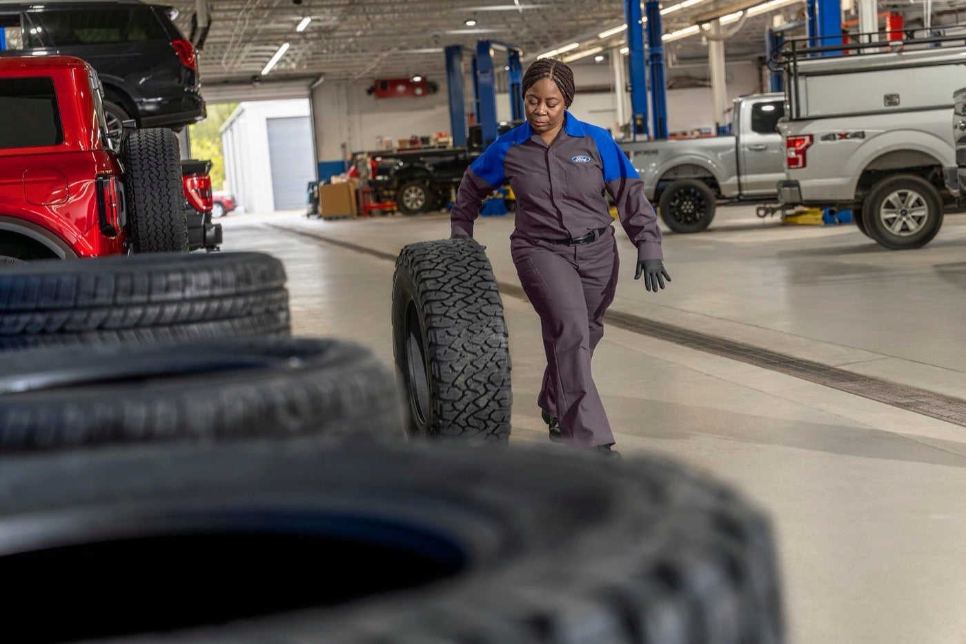 Ford Service technician rolling a new tire toward a vehicle