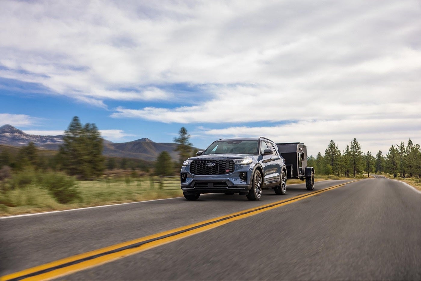 Ford Explorer towing a travel trailer on a highway through hills