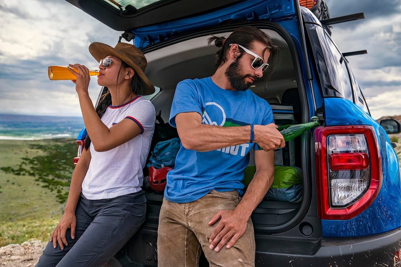 Two people leaning on the tailgate of a Ford Bronco Sport using the built in bottle opener