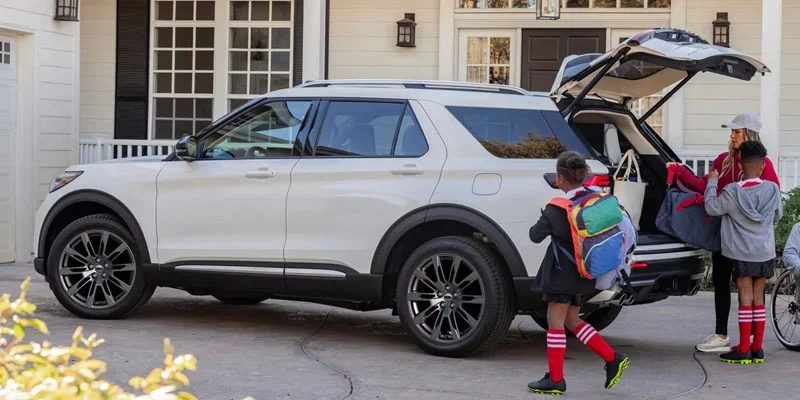 White SUV parked in a driveway with people loading items into the rear cargo area.